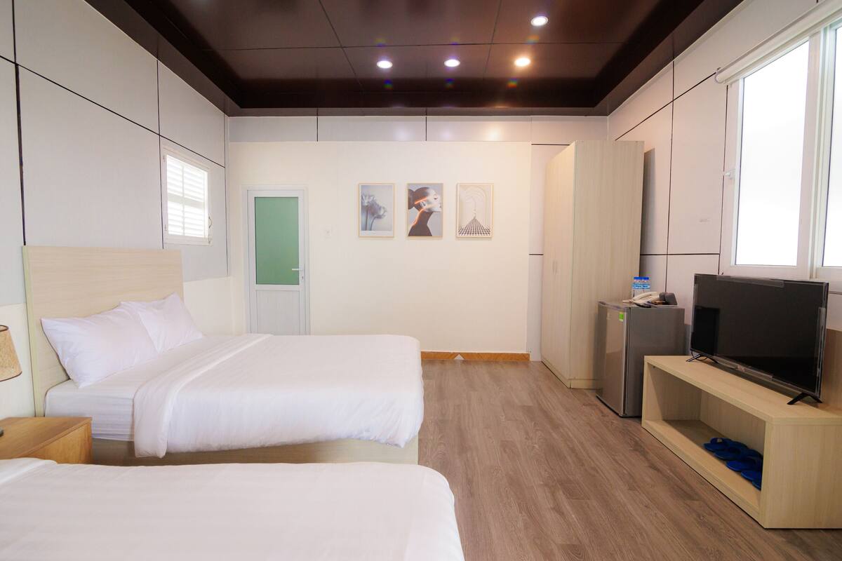 A hotel room with two beds, a television, a small refrigerator, and artwork on the wall.