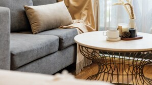 A living room with a grey sofa, a round coffee table, and a curtain with vertical lines. - TTR Vincent Hotel (Xuan Huong - Da Lat)