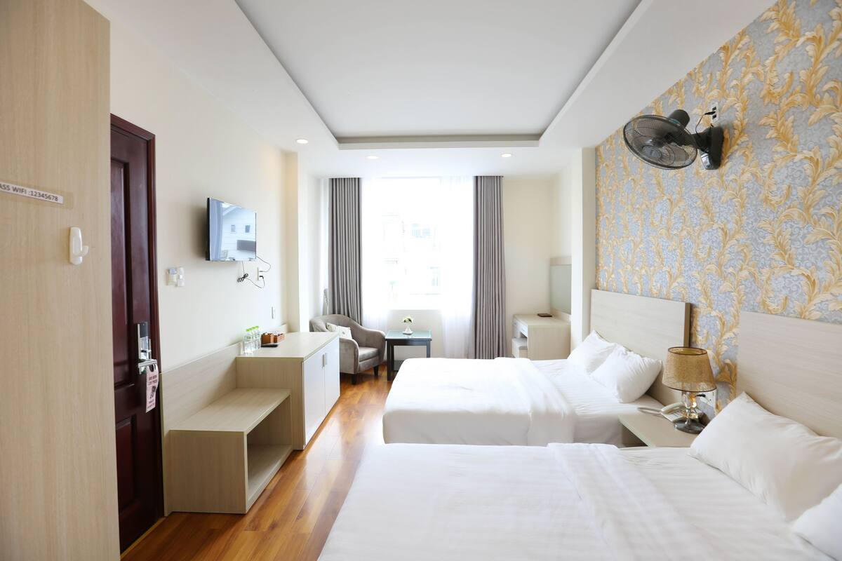 A hotel room with two beds, a desk, a chair, a TV, and a window with curtains.