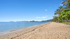 A wide sandy beach with clear blue water and distant mountains. - Alassio 2 Bedroom Direct Pool Access104 (Palm Cove)