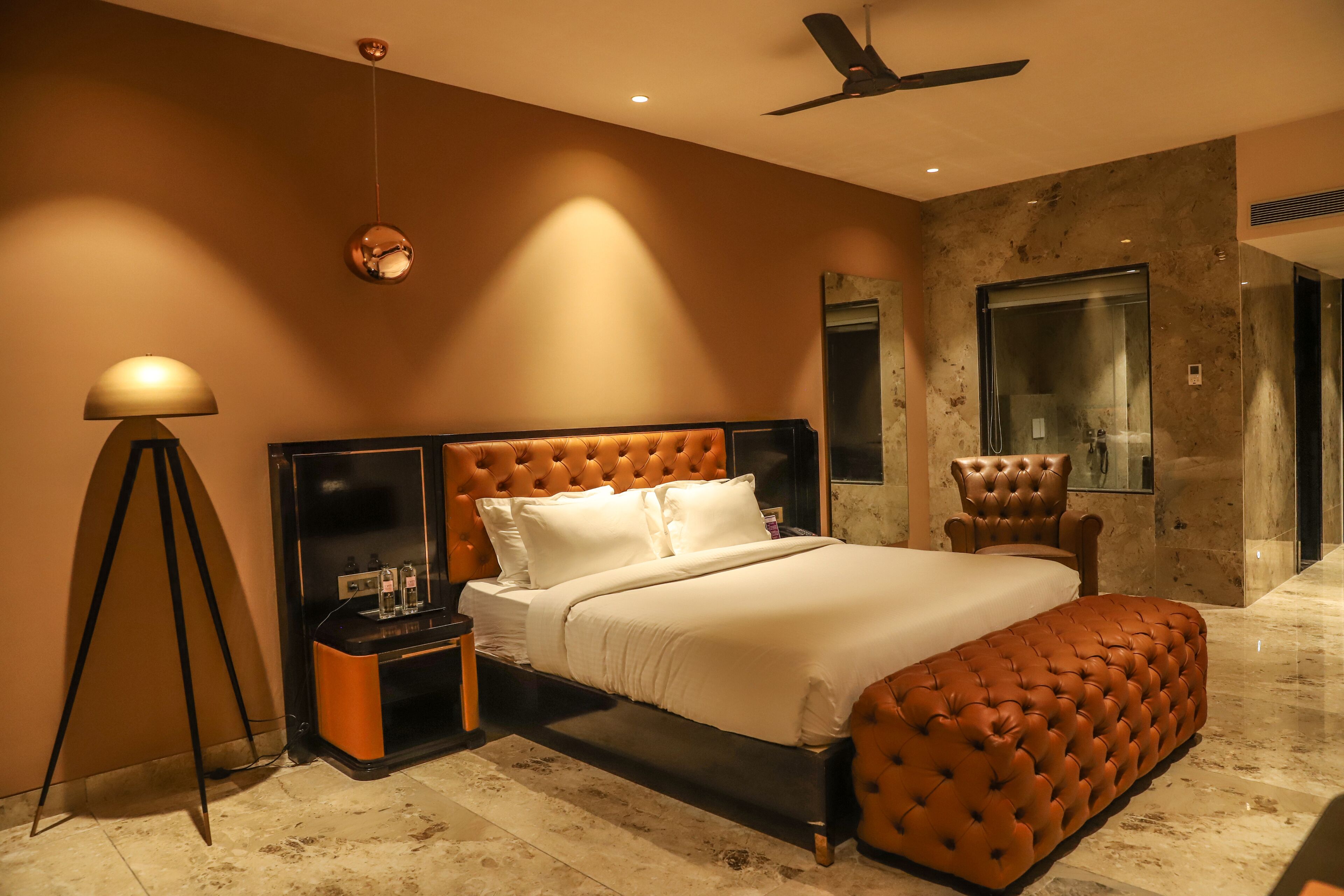 A modern bedroom with a tufted headboard, a large bed, a standing lamp, and a ceiling fan.