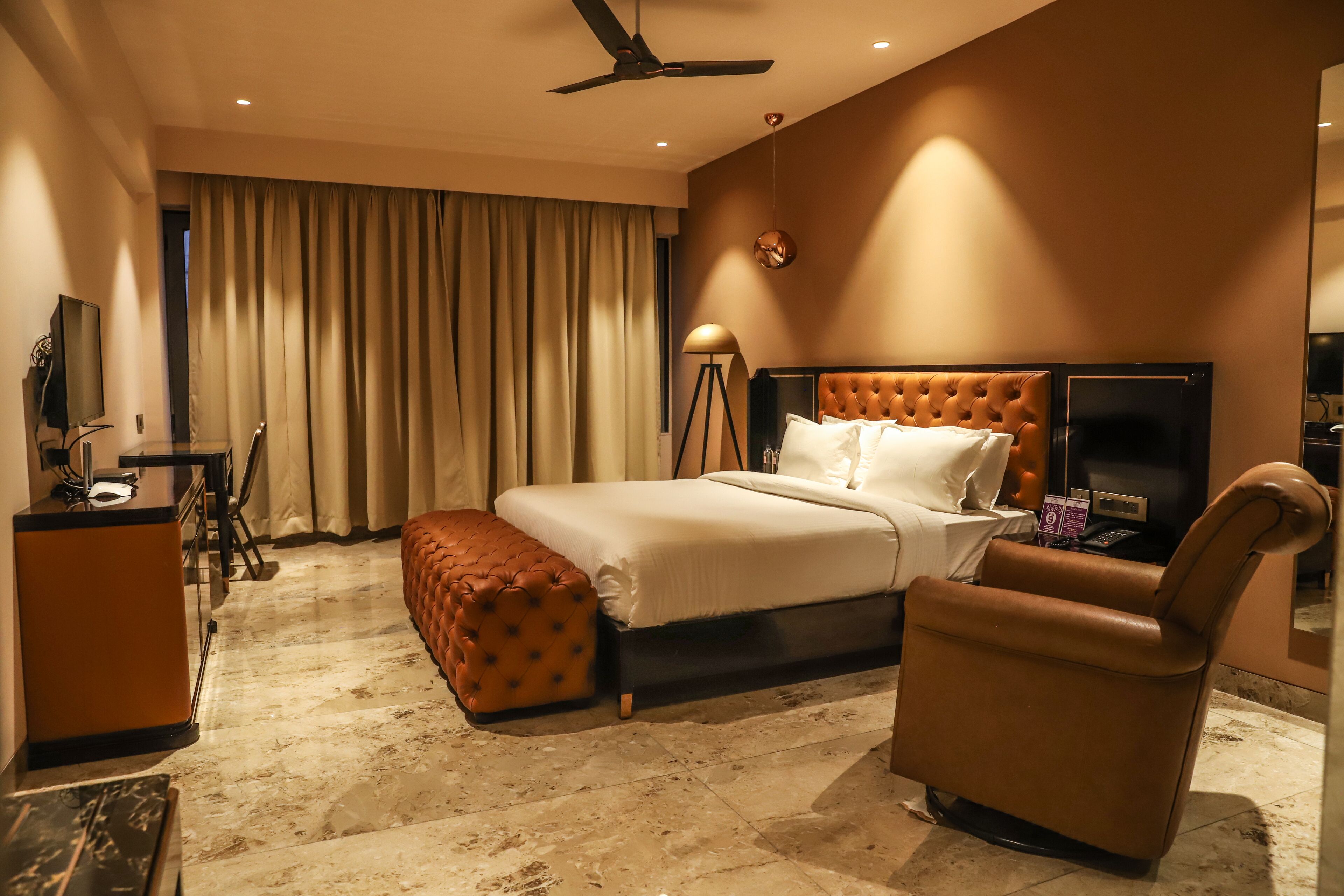 A hotel room with a large bed, a desk, a chair, a television, and a ceiling fan.