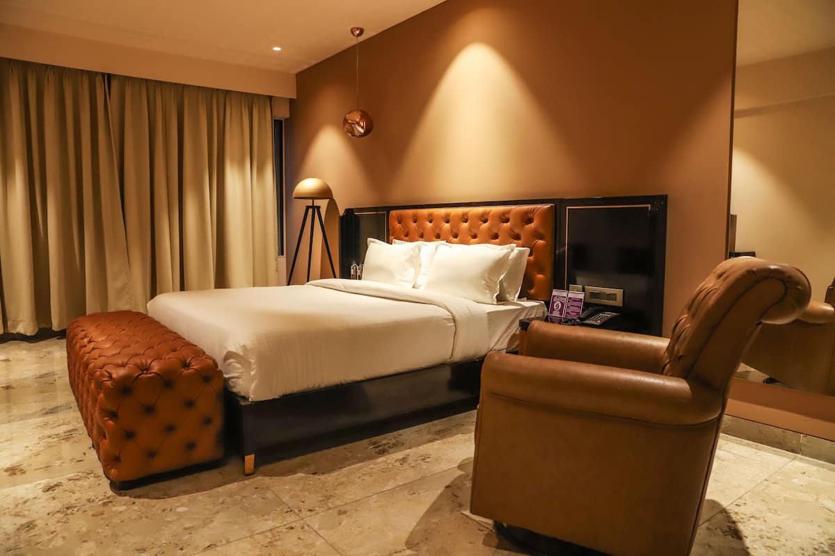 A hotel room with a large bed, a chair, a lamp, and a mirror.