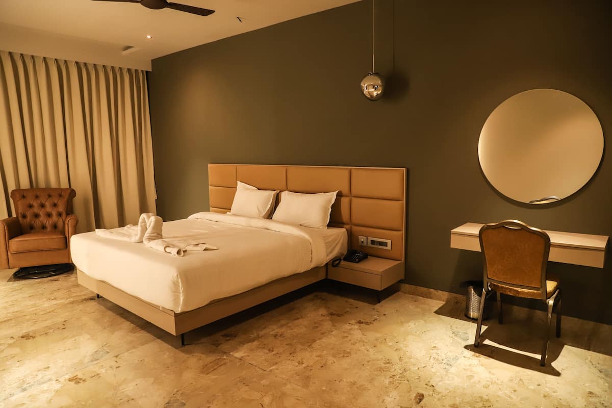 A hotel room with a large bed, a desk, a chair, a round mirror, and a ceiling fan.