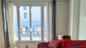 Een woonkamer met een glazen salontafel, een rode bank en een uitzicht op gebouwen door grote ramen.