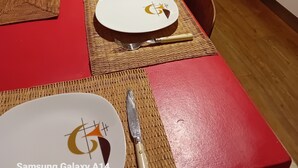 Een eettafel gedekt met borden, bestek en placematen in een kamer met houten vloeren en een keukenhoek.