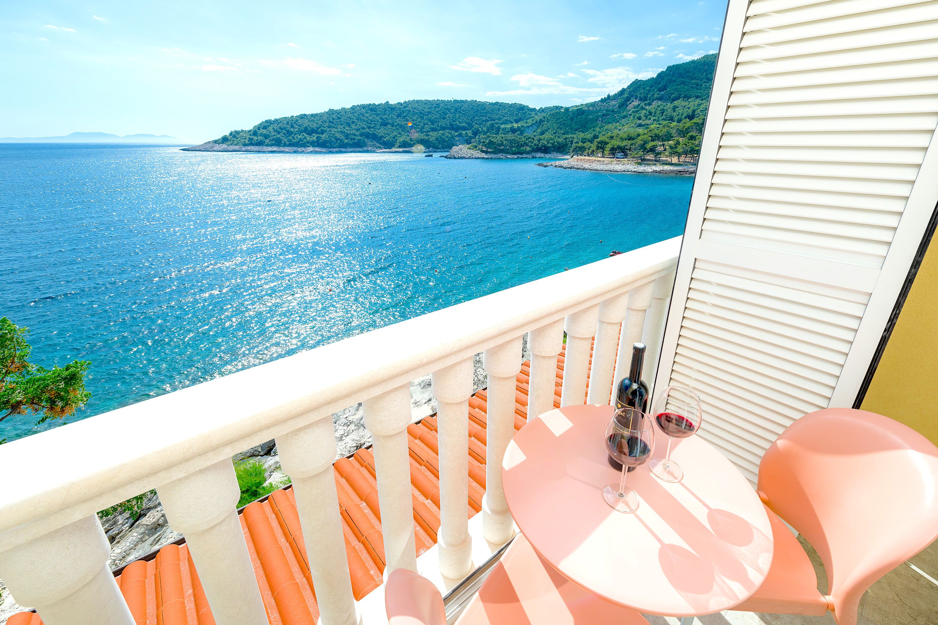 A balcony with a table and chairs overlooking a sea view.