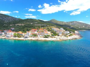 A coastal town with buildings along the shoreline, clear blue waters, and hilly terrain in the background. - Apartments Mario Tudor (Hvar)