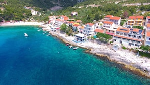 Une ville côtière avec des bâtiments qui bordent le littoral, une eau d’un bleu limpide et un paysage montagneux en arrière-plan.