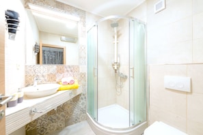 A bathroom with a glass-enclosed shower, a sink with a mirror, and patterned tiles. - Apartments Mario Tudor (Hvar)
