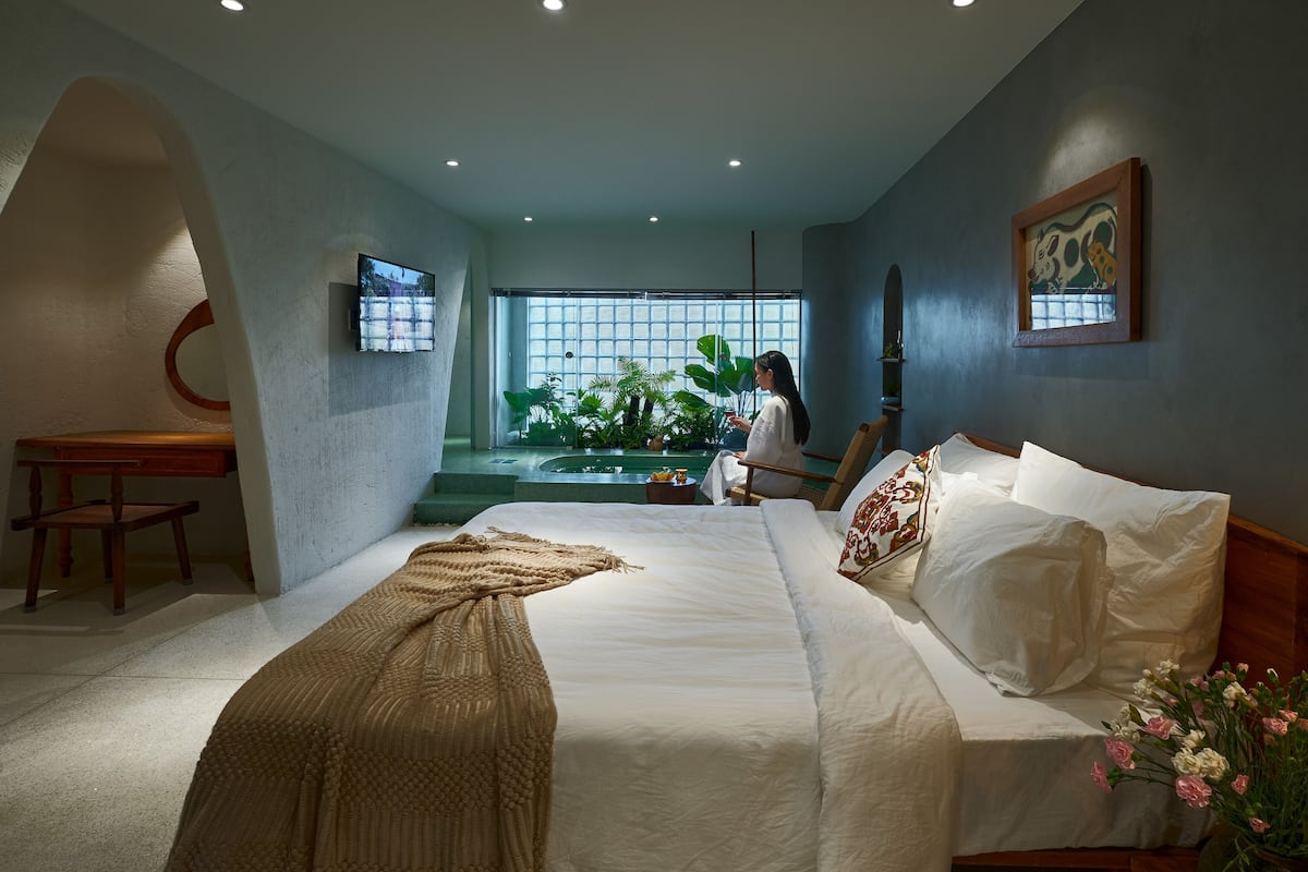 Un dormitorio moderno con cama, escritorio, silla, ventana con vistas a la vegetación y un cuadro en la pared.