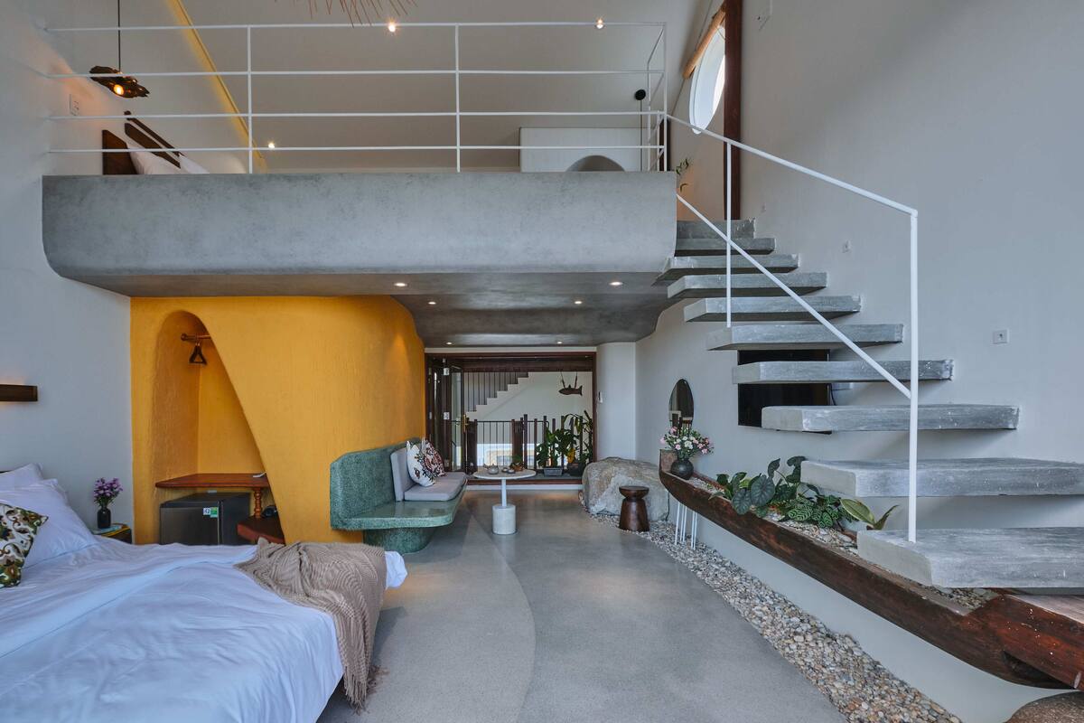 Una habitación de hotel moderna con una cama grande, un sofá, una zona de comedor y una escalera.