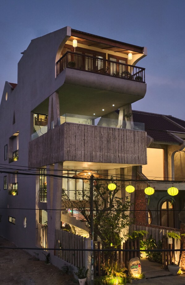 Un edificio moderno de varios pisos con un balcón en el nivel superior, ventanas amplias y una valla de madera al frente.