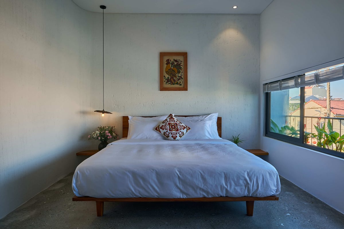 Un dormitorio moderno con una cama grande, cabecera de madera, lámpara colgante y una ventana con persianas.