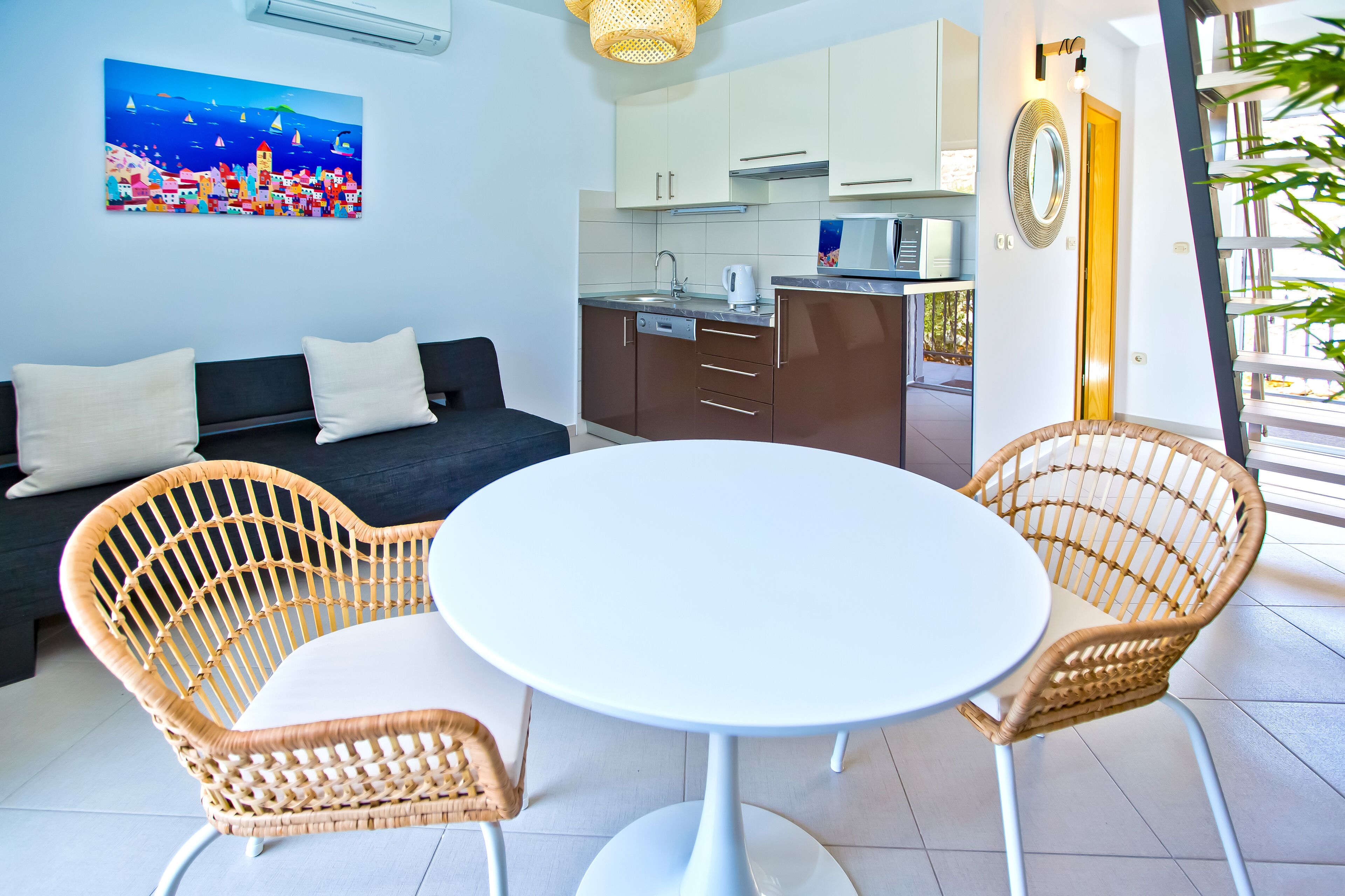 A modern living room with a round table, wicker chairs, a sofa, and a kitchen in the background.