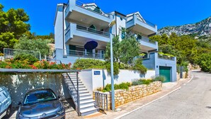 A modern two-story building with balconies, a staircase, and a stone wall. - Apartments Maslina (Hvar)