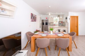 A dining area with a wooden table set for four, surrounded by four chairs. A flat-screen TV is mounted on the wall to the left.