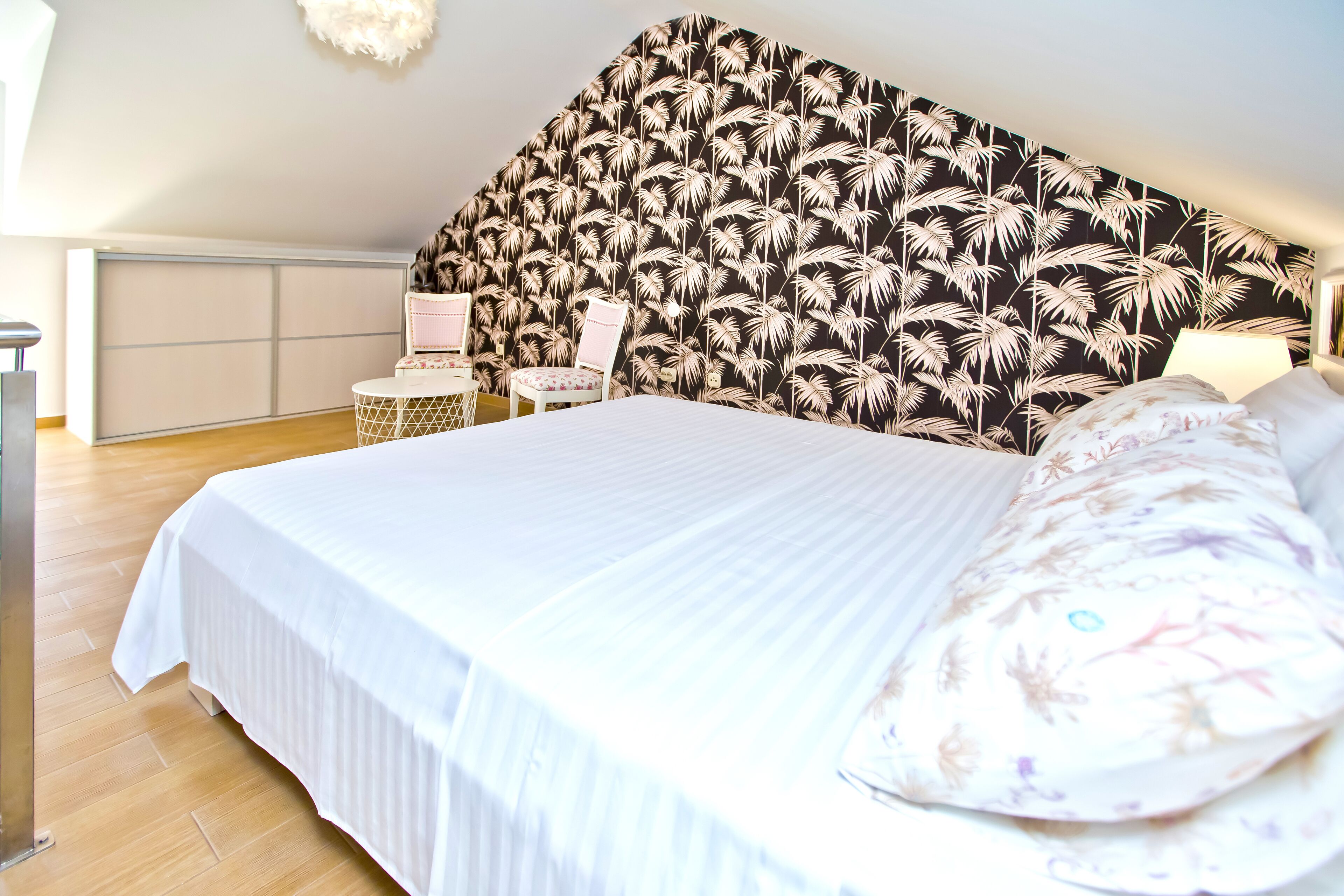 A bedroom with a bed, a nightstand, a chair, and a wall with a leaf pattern.