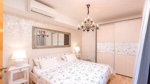 A bedroom with a large bed, a nightstand with a lamp, a dresser, a mirror, and a wardrobe. - Apartments Maslina (Hvar)