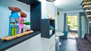 A modern interior with a wooden shelf displaying colorful painted objects, a minimalist dining area, and a view of the outdoors. - Apartments Maslina (Hvar)