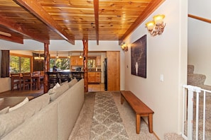 A spacious living area with a wooden ceiling, a stone-patterned rug, a sofa, and a bench. - Golden Bear Pines by Destination Big Bear: Walk to Snow Summit! Fenced Yard! Pet Friendly! HOT TUB! (Big Bear Lake)