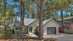 A two-story house with a garage, surrounded by tall pine trees.