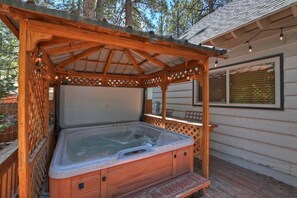 Un jacuzzi bajo una pérgola de madera con vistas a una casa al fondo.