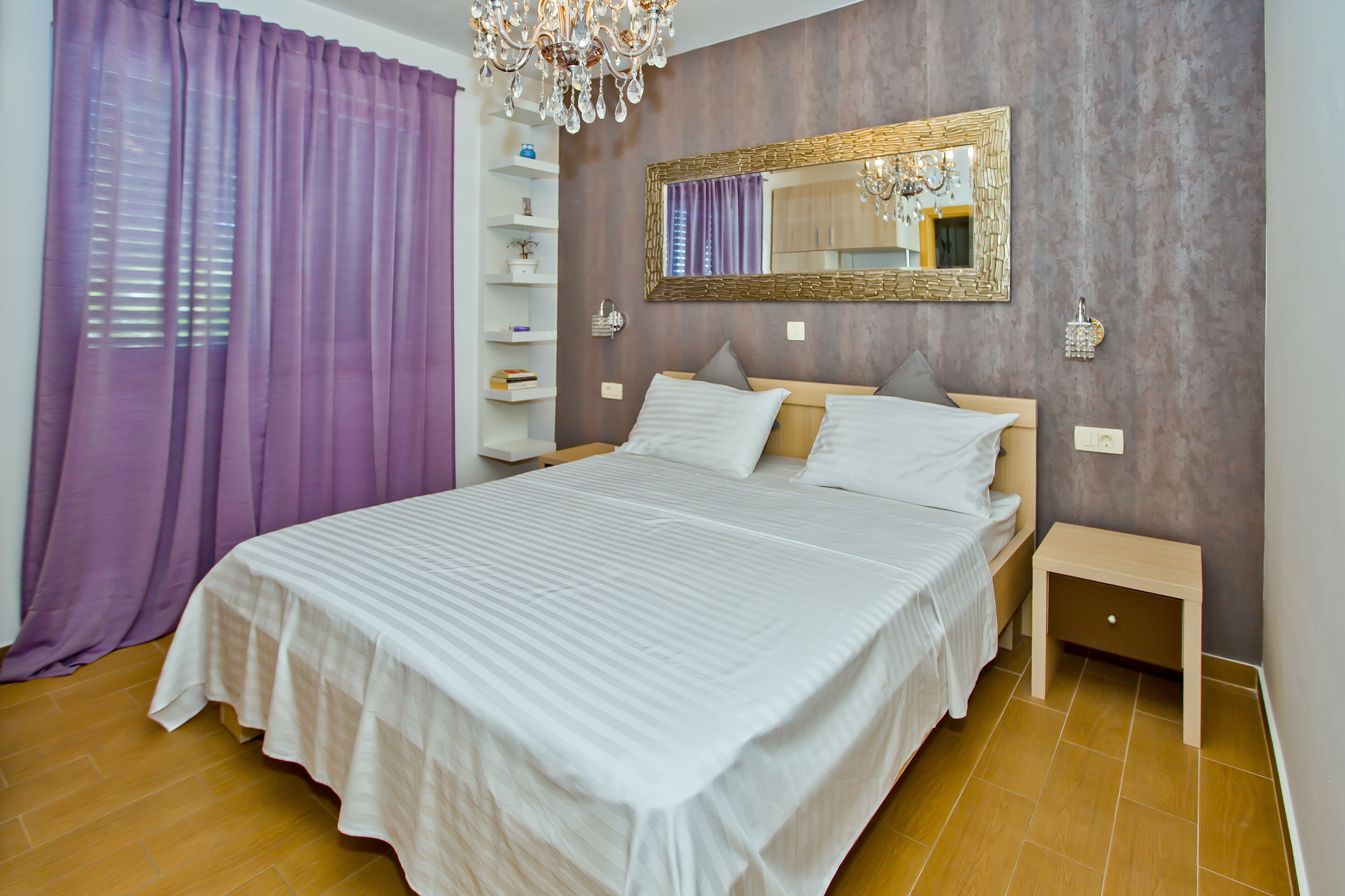 A bedroom with a large bed, a bedside table, a nightstand, a wardrobe, and a mirror on the wall.