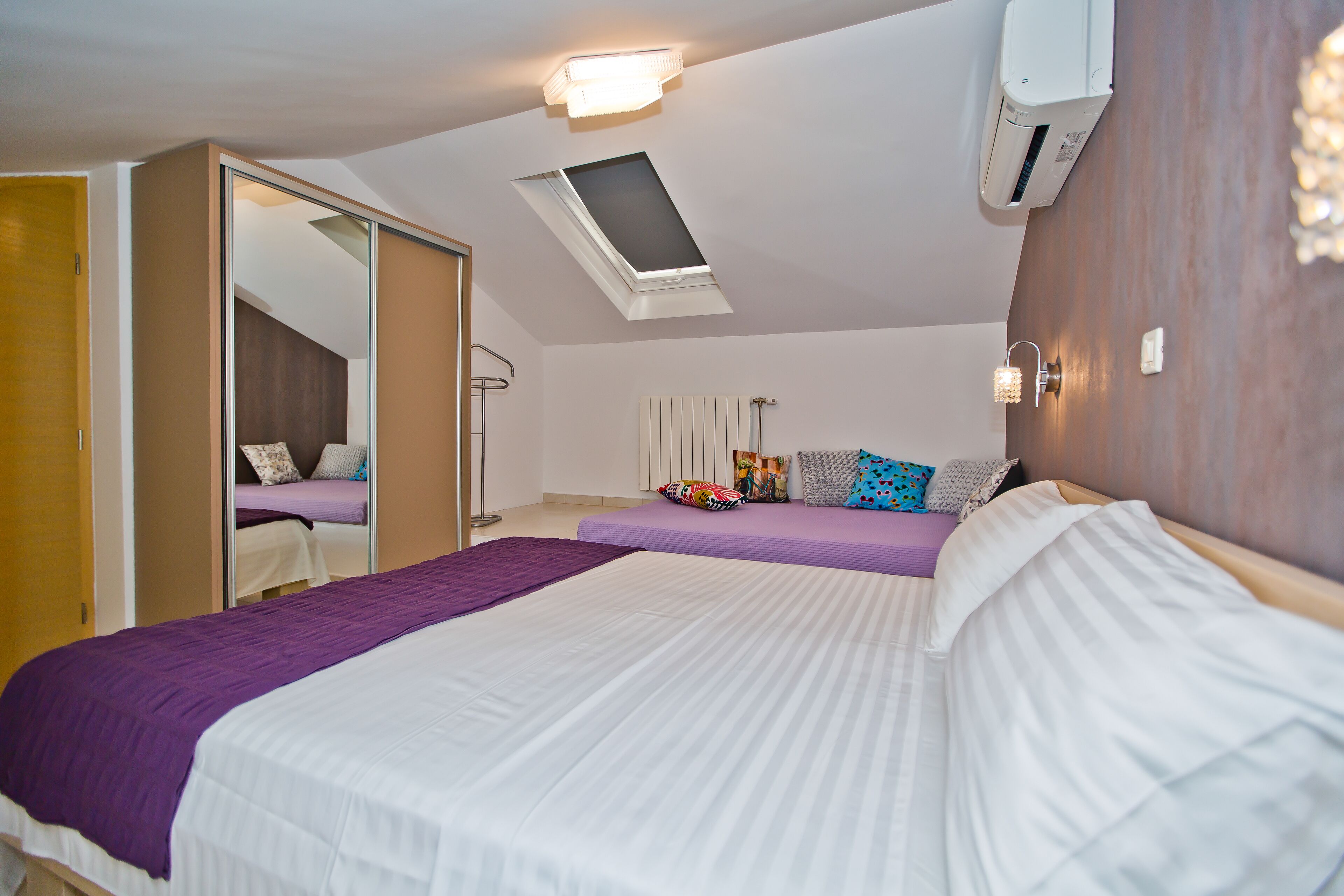 A bedroom with a large bed, a smaller bed, a skylight, and an air conditioning unit.