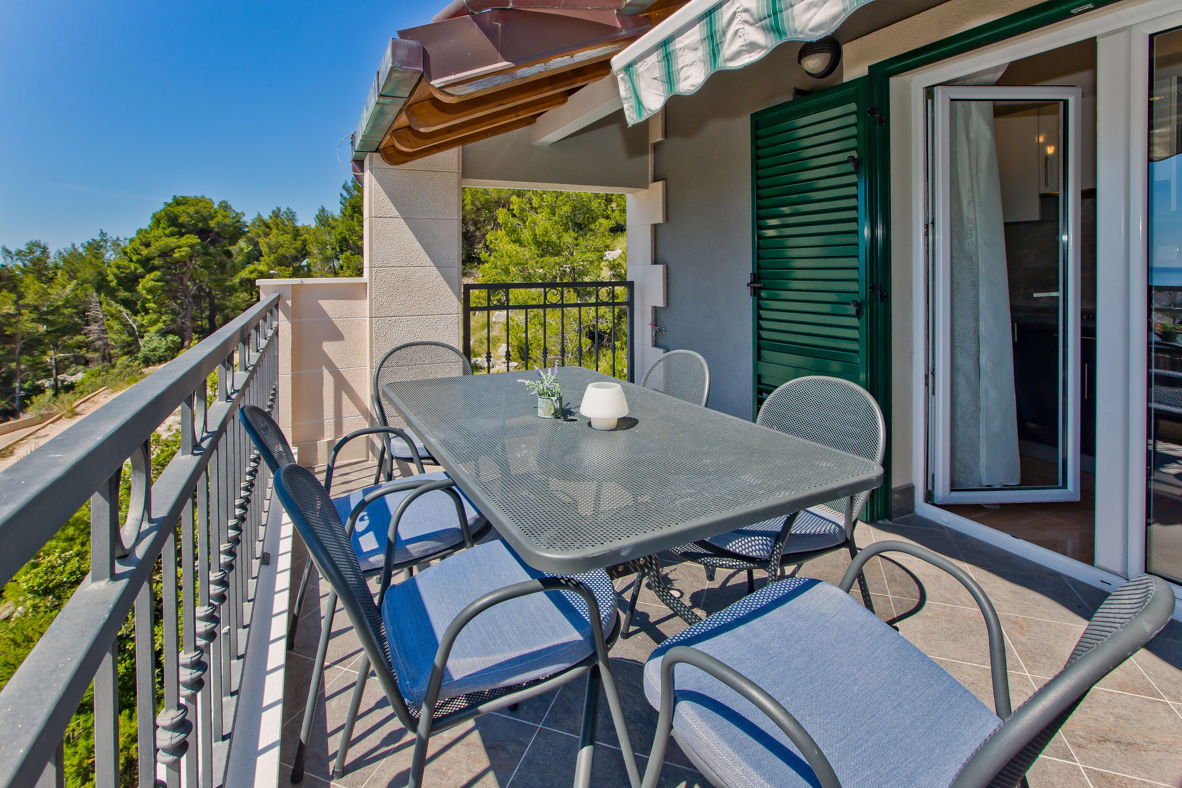 A balcony with a table and chairs, a sliding glass door, and a view of trees.
