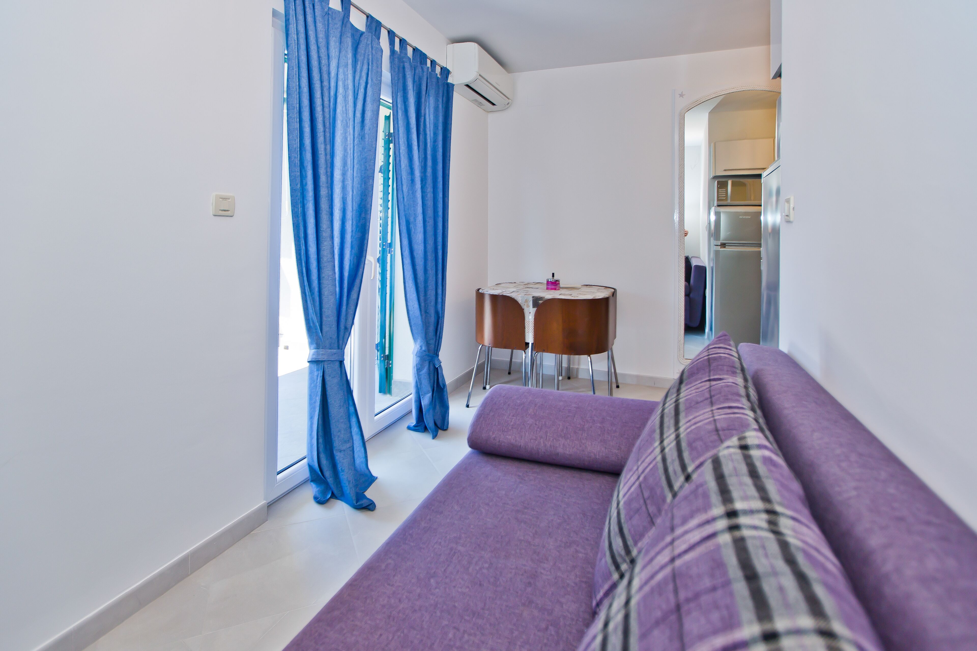 A modern living room with a purple sofa, a small round table, and blue curtains.