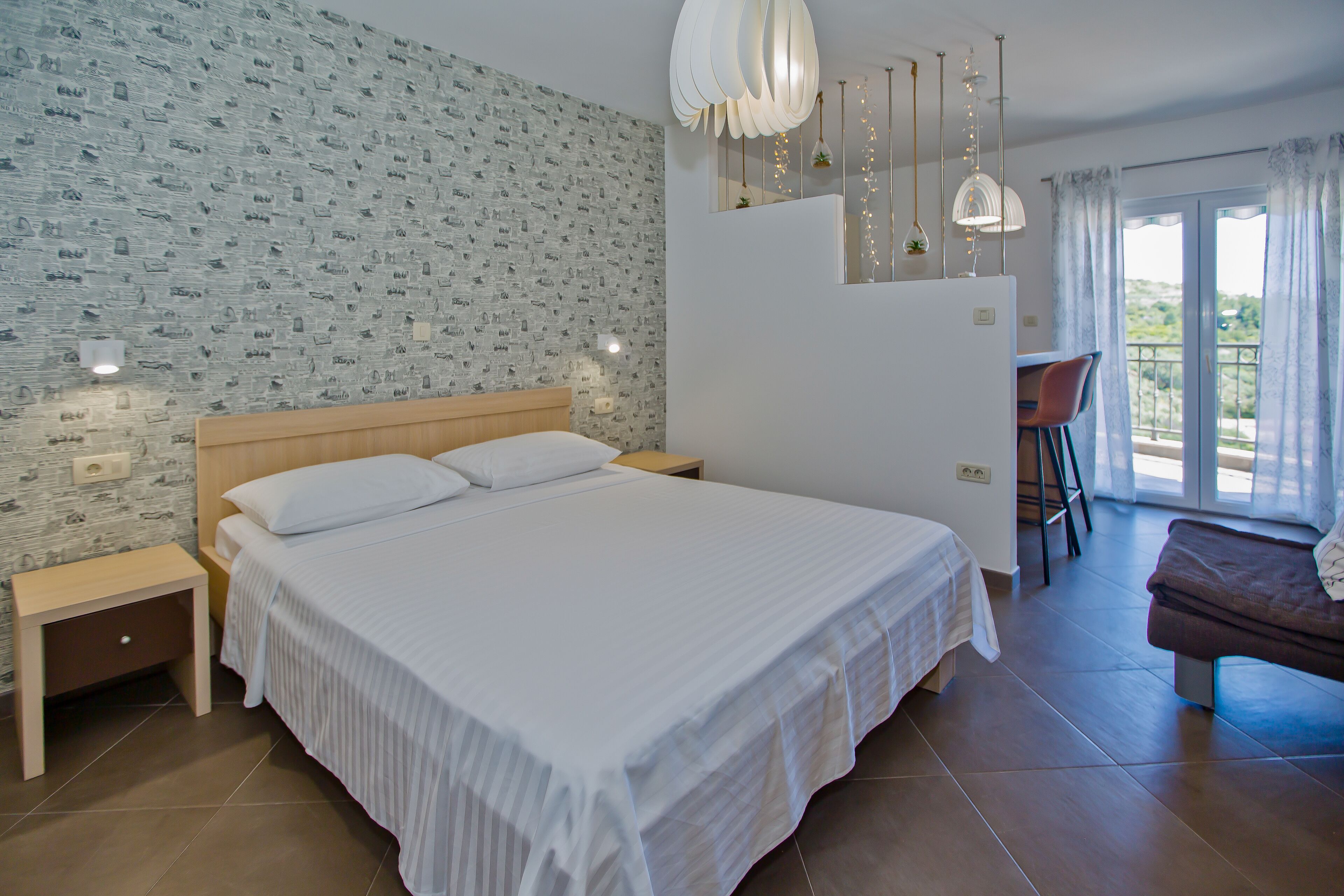 A bedroom with a large bed, a wooden nightstand, a small table, and a chair.