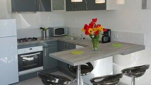 A modern kitchen with grey cabinets, a microwave, a stove, and a sink. There is a vase with red and yellow flowers on the countertop. - Central Apartment in La Roche-Posay with Pool and Terrace (La Roche-Posay)