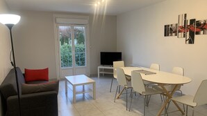 A modern living room with a sofa, a coffee table, a TV, and a dining area with chairs and a table. - Central Apartment in La Roche-Posay with Pool and Terrace (La Roche-Posay)