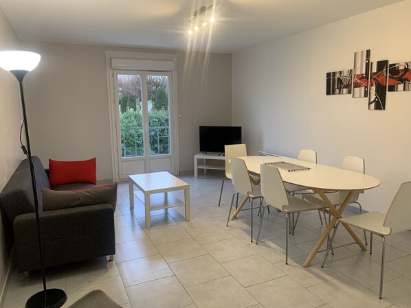 A modern living room with a sofa, a coffee table, a TV, and a dining area with chairs and a table. - Central Apartment in La Roche-Posay with Pool and Terrace (La Roche-Posay)