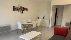 A modern living room with a dining area, a grey sofa with red cushions, and a white table. - Central Apartment in La Roche-Posay with Pool and Terrace (La Roche-Posay)