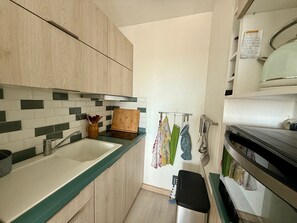 A kitchen with a sink, wooden cabinets, a cutting board, and hanging kitchen towels.
