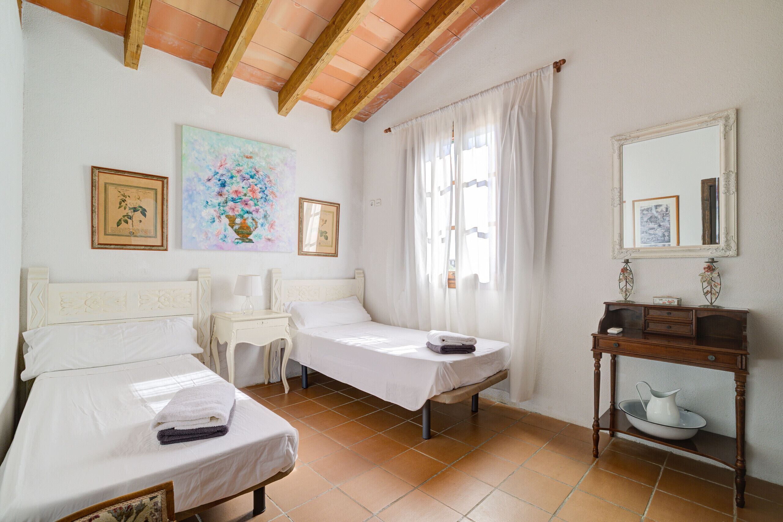 A bedroom with two beds, a bedside table, a nightstand, a mirror, and a painting on the wall.