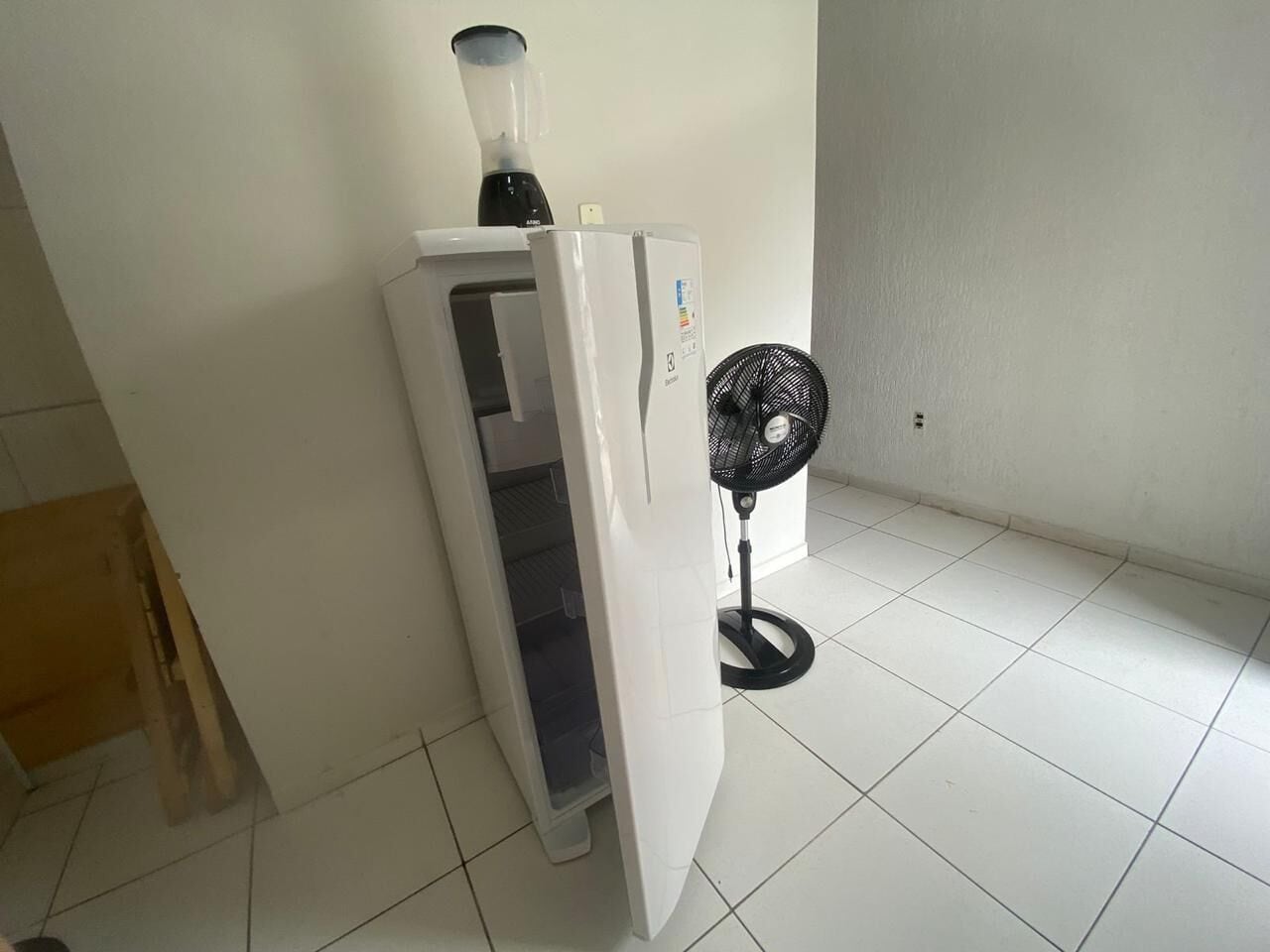 Une petite pièce avec un réfrigérateur blanc, un ventilateur noir et une porte en bois.
