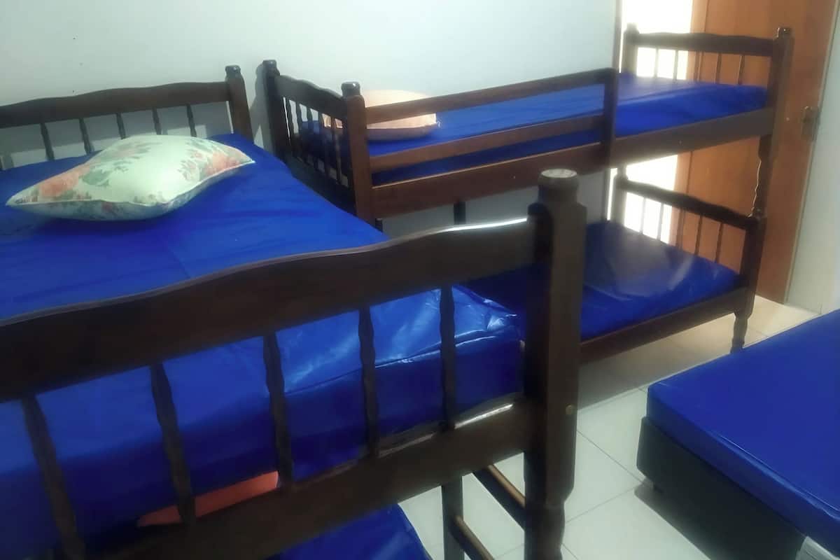 Une chambre avec des lits superposés et un lit simple, des têtes de lit en bois et un coussin à motifs floraux sur l’un des lits.