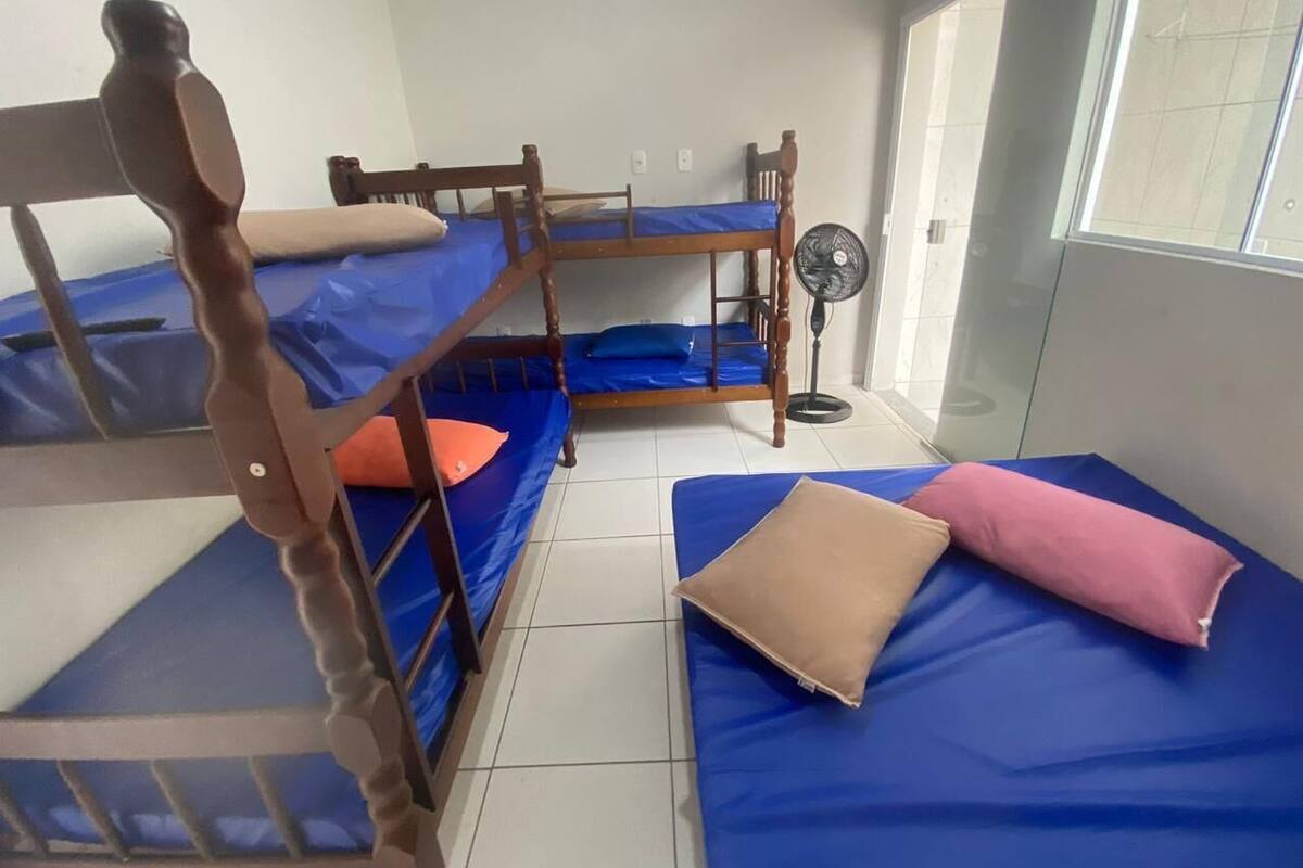 Une chambre de dortoir avec des lits superposés, un ventilateur sur pied et une fenêtre donnant sur un paysage agréable.