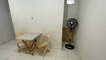 A small room with a wooden table and chairs, a standing fan, and a window.