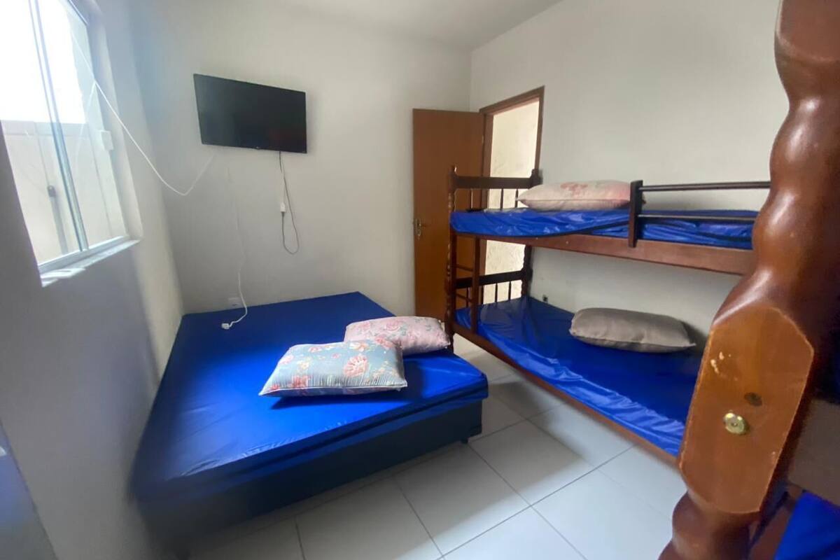 Une chambre de dortoir avec des lits superposés, un téléviseur fixé au mur et une fenêtre laissant entrer la lumière naturelle.
