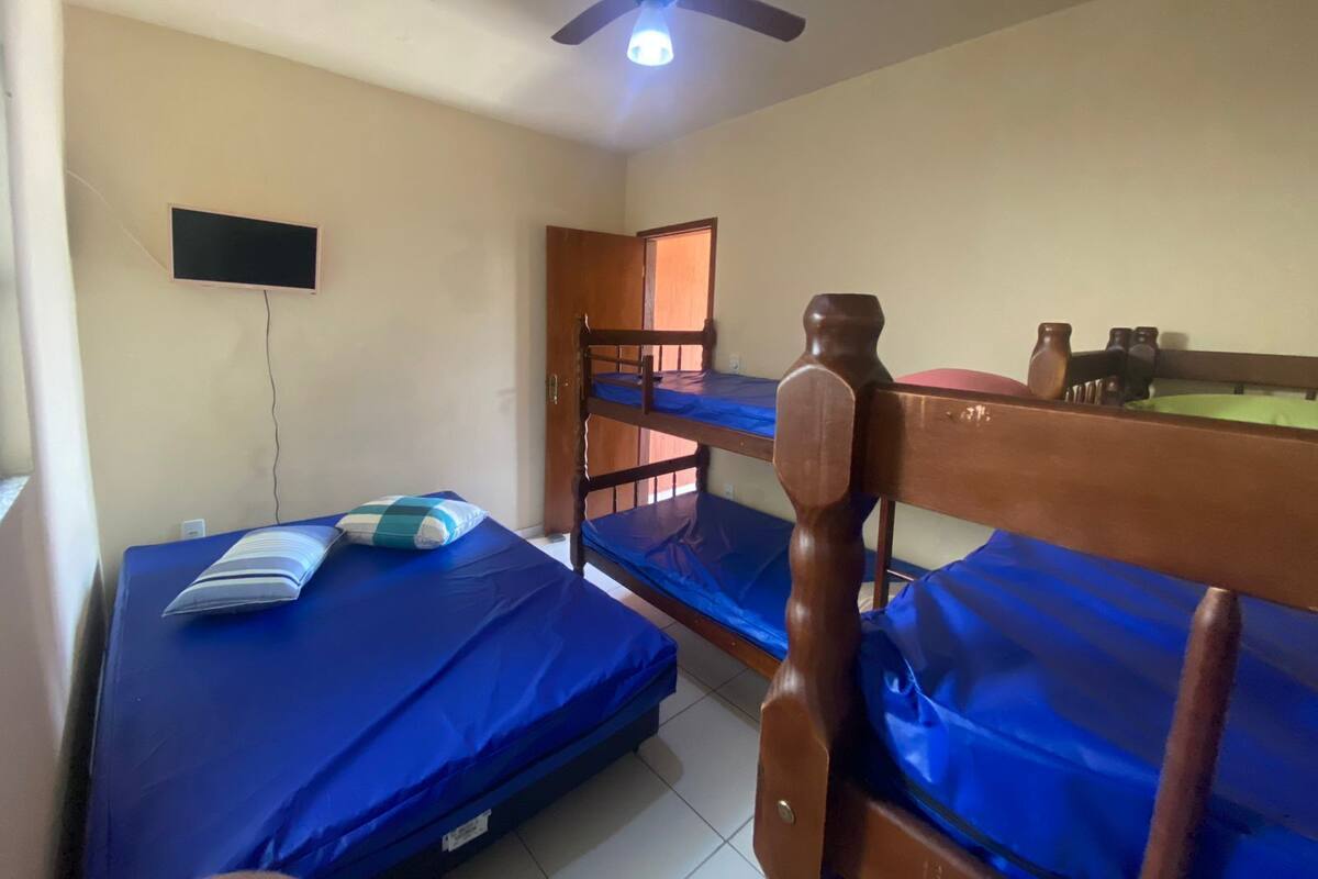 Une chambre de dortoir avec des lits superposés, un ventilateur de plafond, un téléviseur fixé au mur et une porte donnant sur une autre pièce.