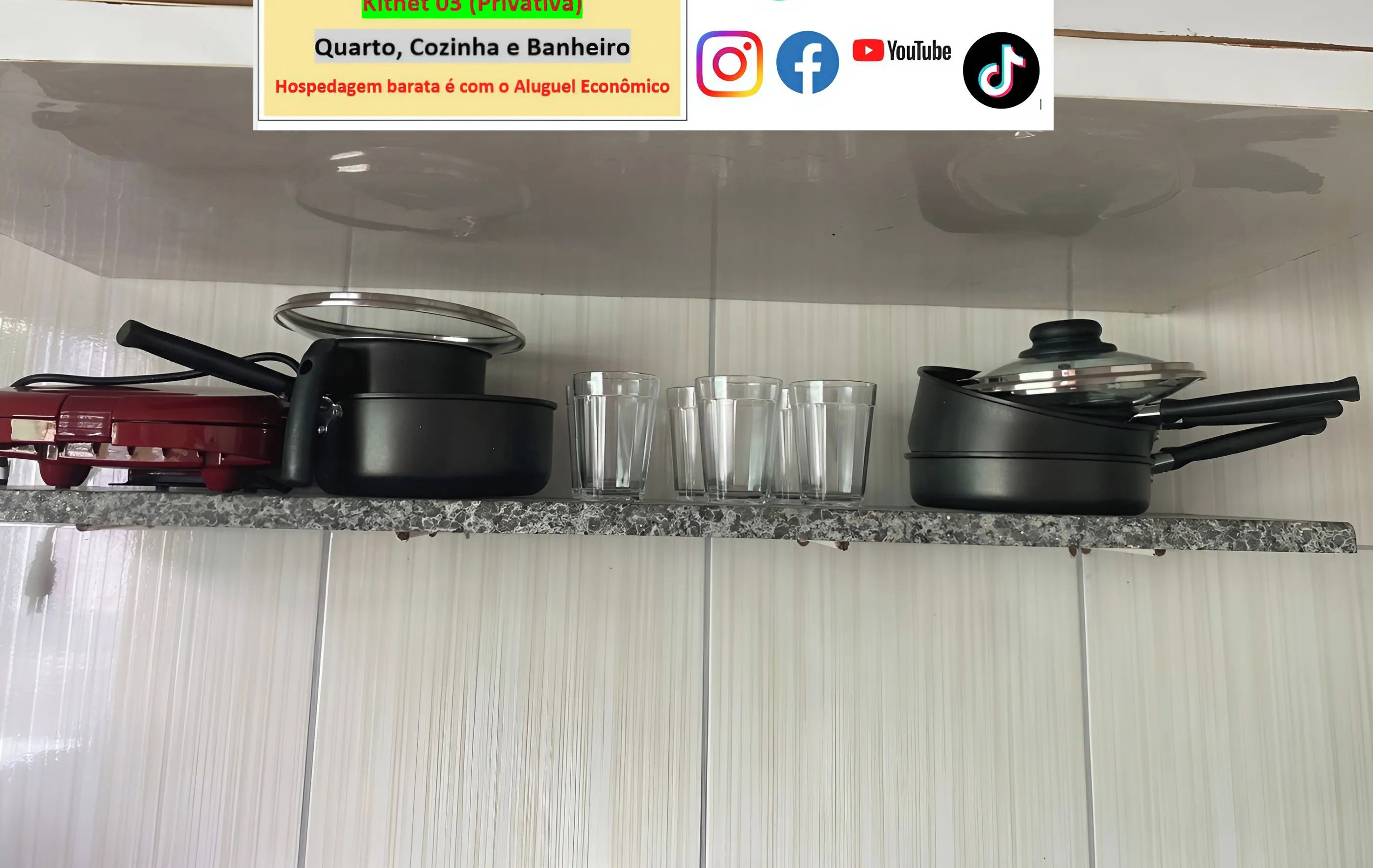 Uma bancada de cozinha com uma panela preta, um eletrodoméstico vermelho e quatro copos de vidro.