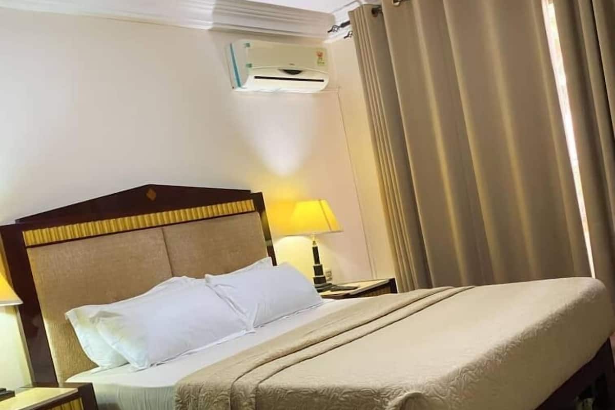 A hotel room with a bed, a bedside table, a lamp, and a window with curtains.