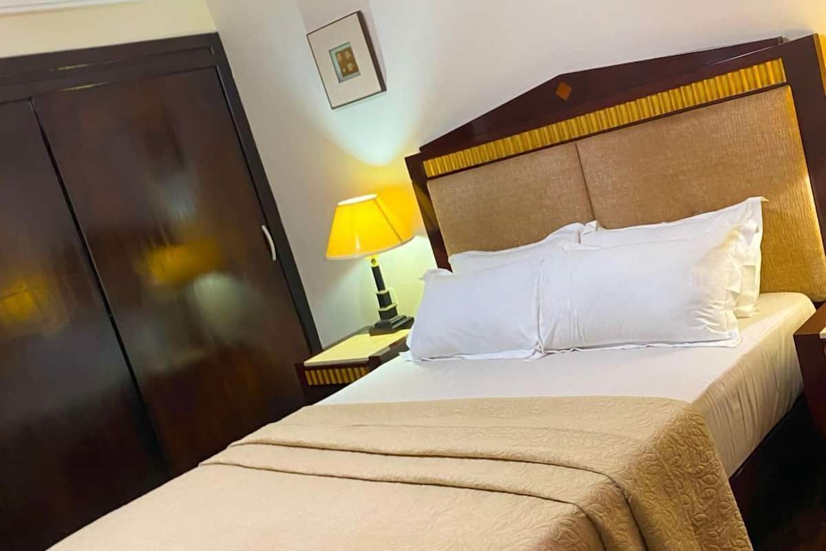 A hotel room with a bed, a nightstand with a lamp, a wardrobe, and a picture on the wall.