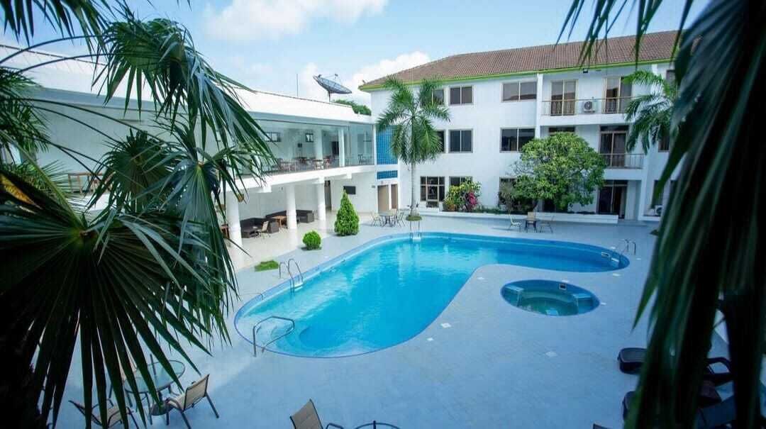 A swimming pool surrounded by palm trees and a building with multiple balconies.