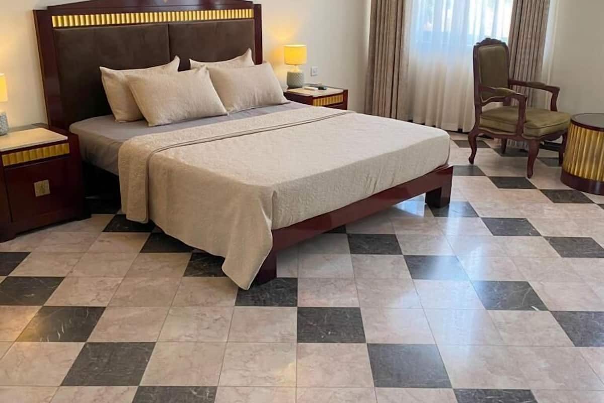 A hotel room with a large bed, a nightstand, a chair, and a small table.
