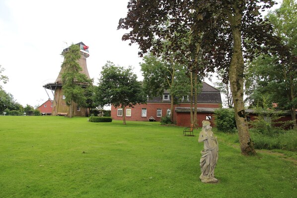 A grassy area with a statue, a red brick building, and a tower with a red roof.